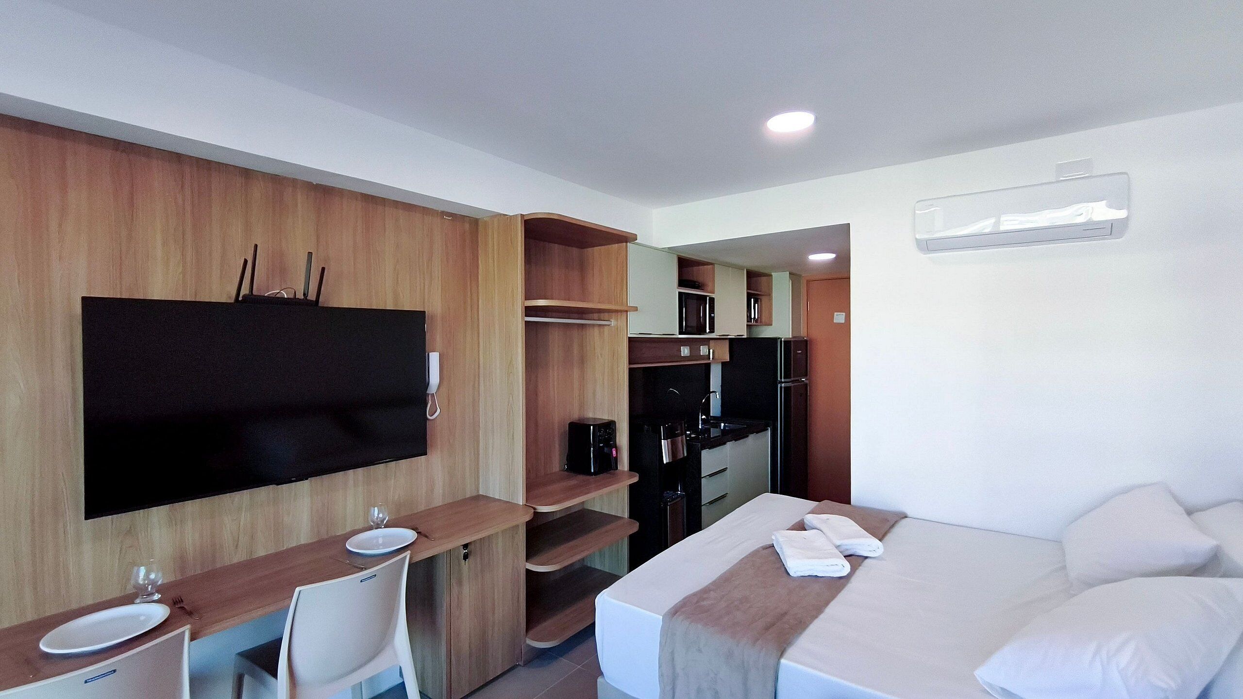 A hotel room with a bed, a desk with a chair, a TV, a microwave, and a refrigerator.