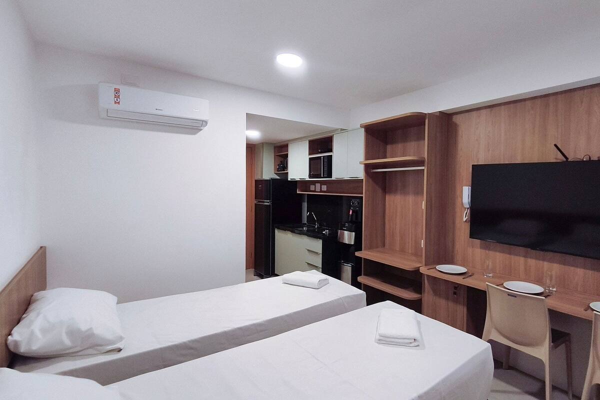 A bedroom with a bed, a TV mounted on the wall, a kitchenette with a microwave, and a closet.