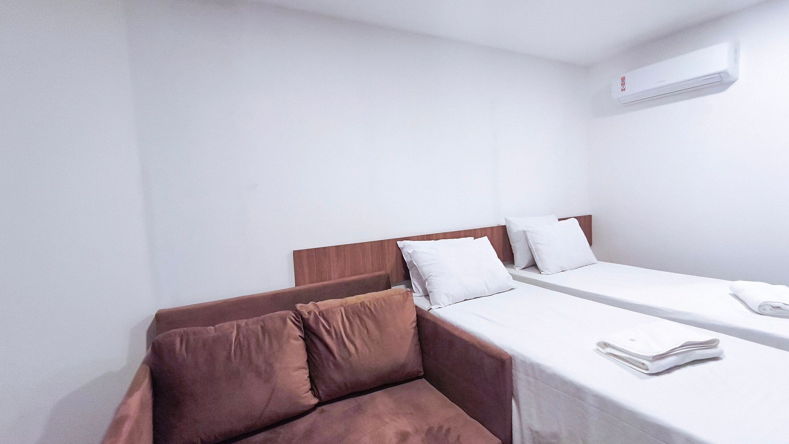 Quarto de hotel com uma cama, um pequeno sofá e uma mesa de cabeceira com uma toalha dobrada.