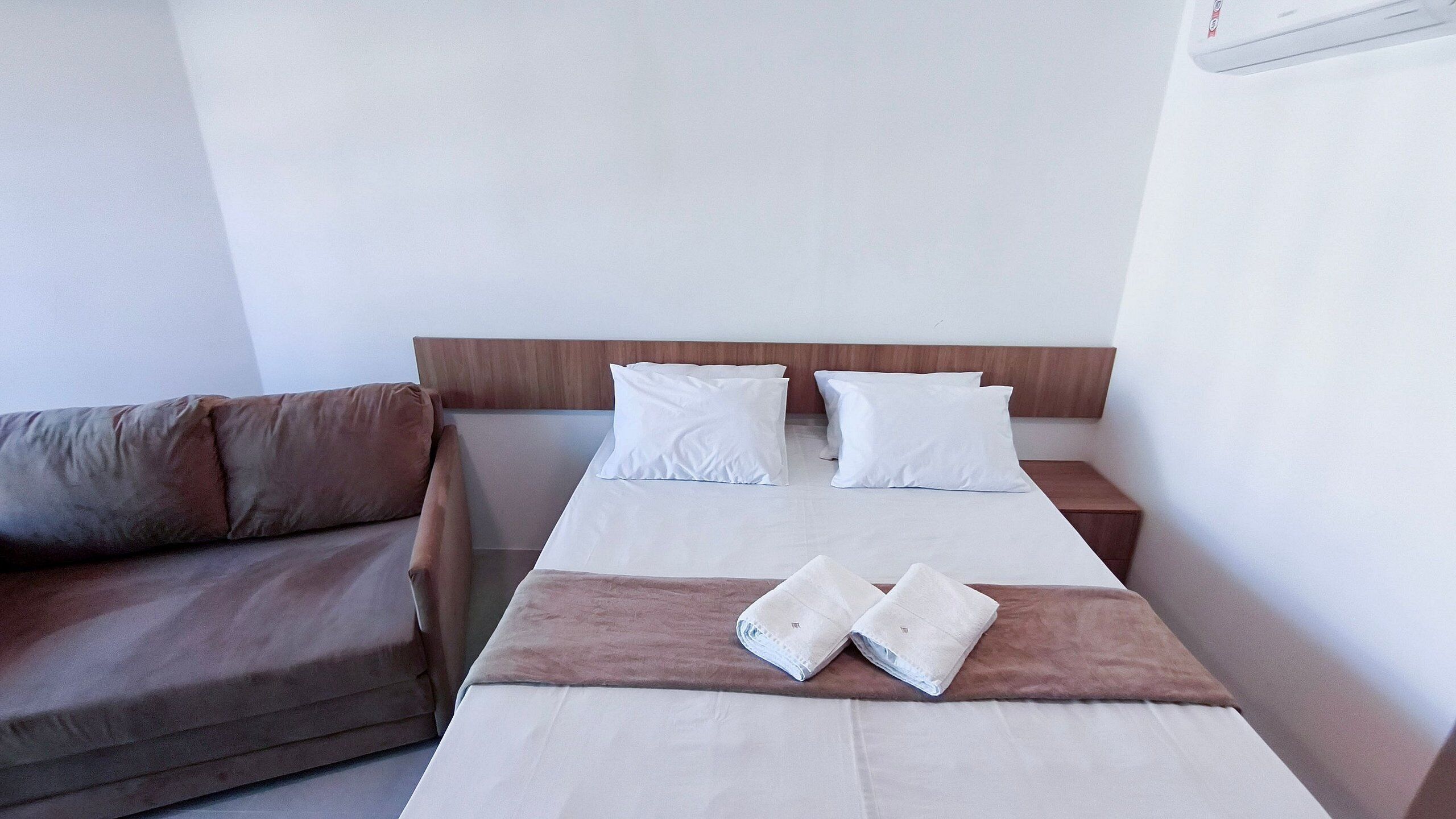 Una cama con sábanas blancas, cabecera de madera y mesita de noche marrón.