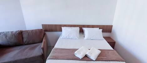 Una cama con sábanas blancas, cabecera de madera y mesita de noche marrón.