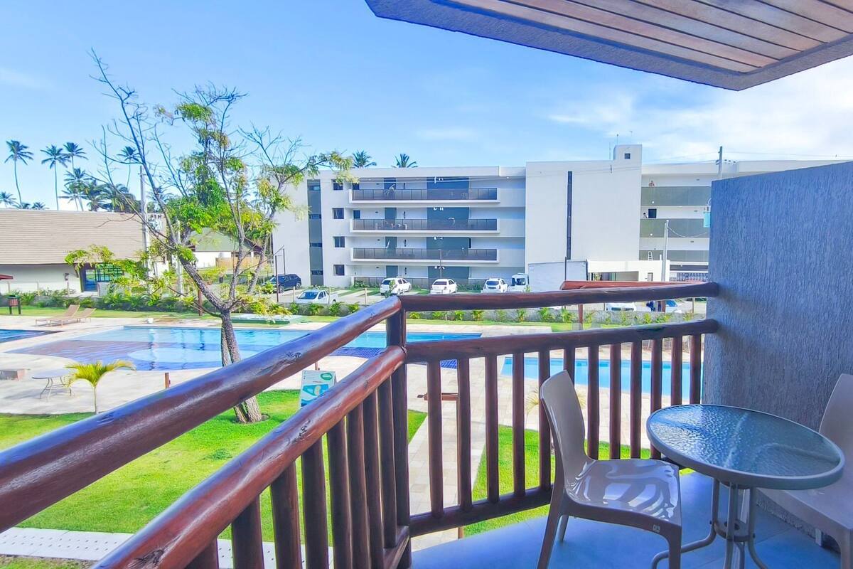 A balcony with a view of a swimming pool, a building in the background, and a table with chairs.