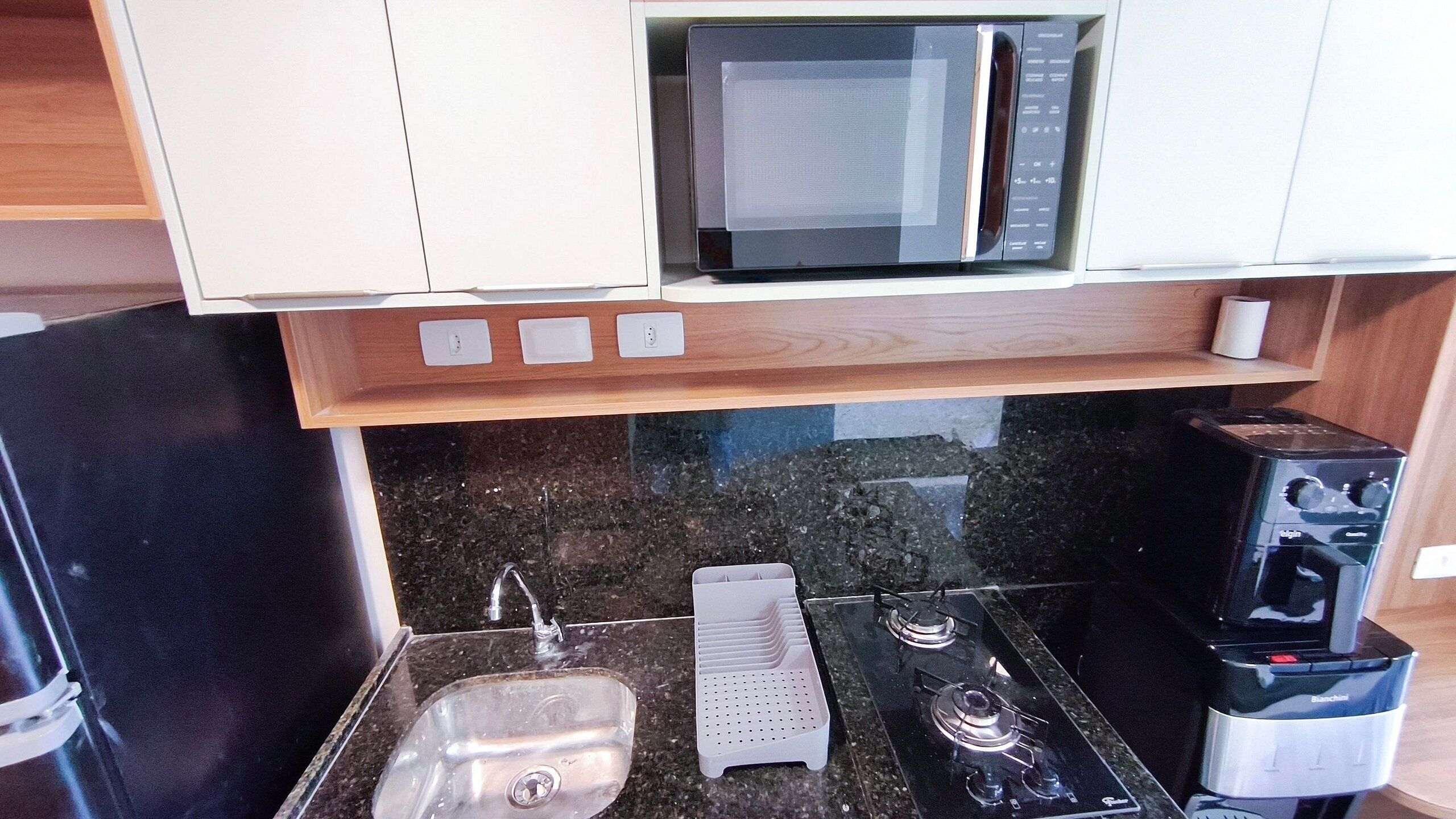 A kitchen with a microwave, stove, sink, and a wooden shelf above.