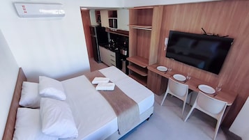 Habitación de hotel con cama, televisión, kitchenette y baño pequeño.
