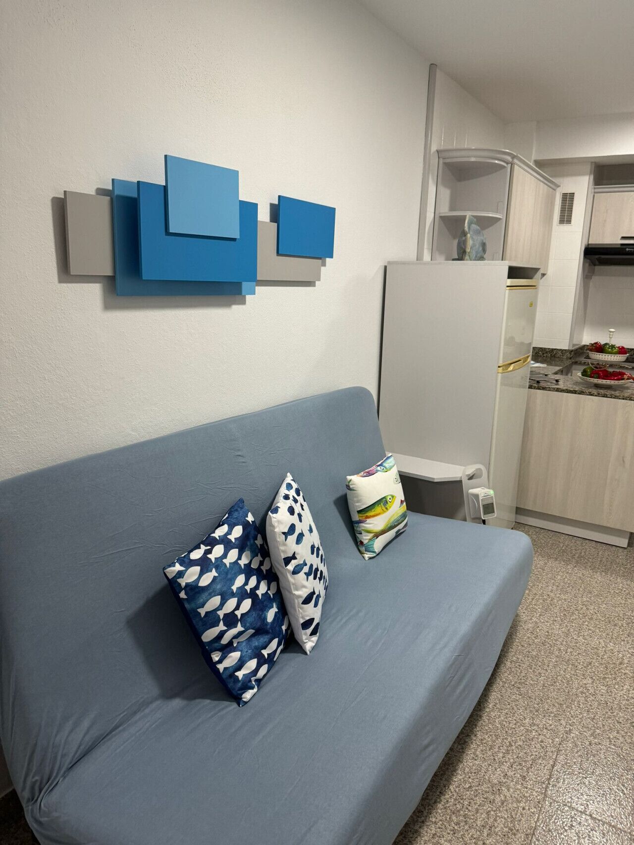 Een moderne woonkamer met een blauwe bank, twee kussens met een patroon en een wanddecoratie in abstractie.
