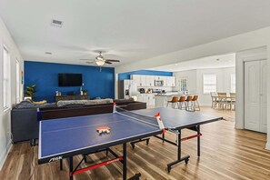 Ett modernt vardagsrum med ett bordtennisbord, en soffa, en tv och ett köksutrymme.