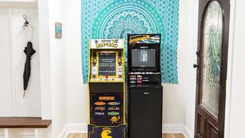 Una máquina recreativa de Pac-Man y un refrigerador Galanz en una habitación con una puerta, un perchero y un tapiz.
