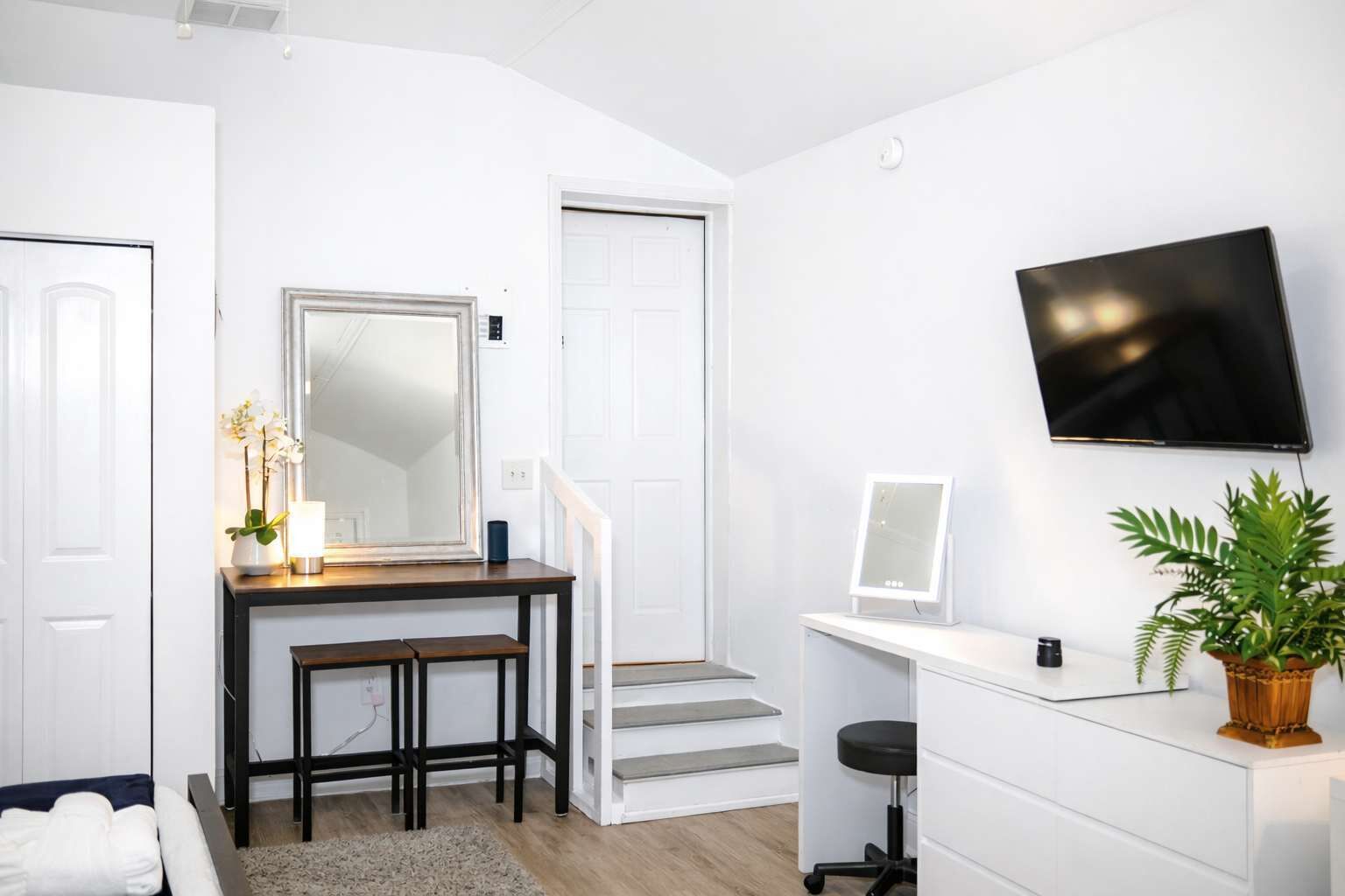 Una habitación moderna y bien iluminada con escritorio, silla y televisión en la pared.