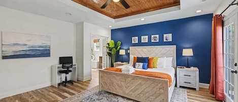 A bedroom with a bed, a desk, a chair, a ceiling fan, and a view of the outdoors.