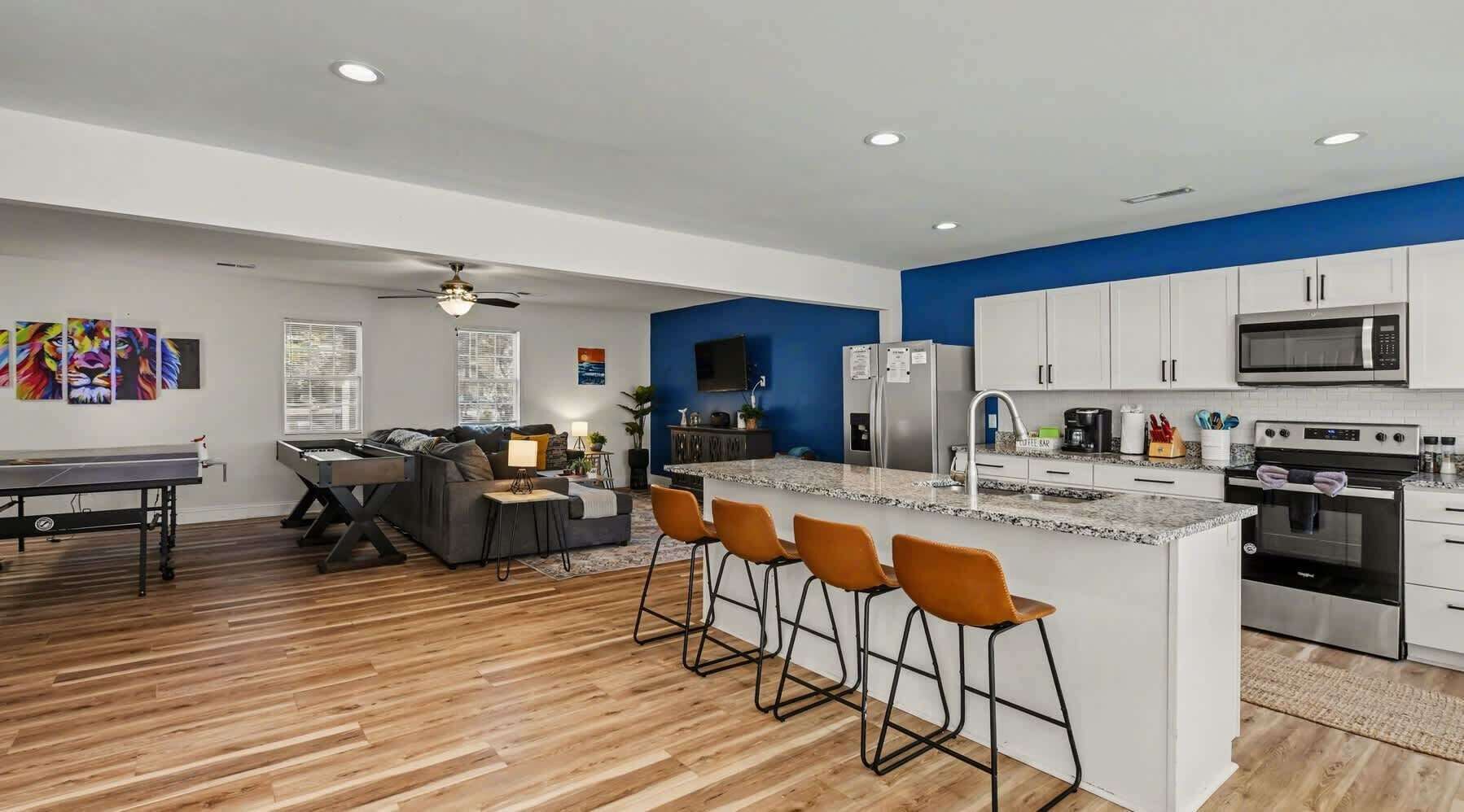 Una cocina moderna con una isla central, taburetes de bar y una zona de comedor con sofá y mesa de centro.