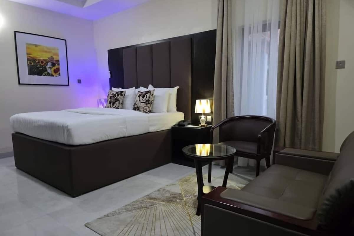 Une chambre d’hôtel moderne avec un grand lit, un canapé, une petite table et une table de chevet avec une lampe.