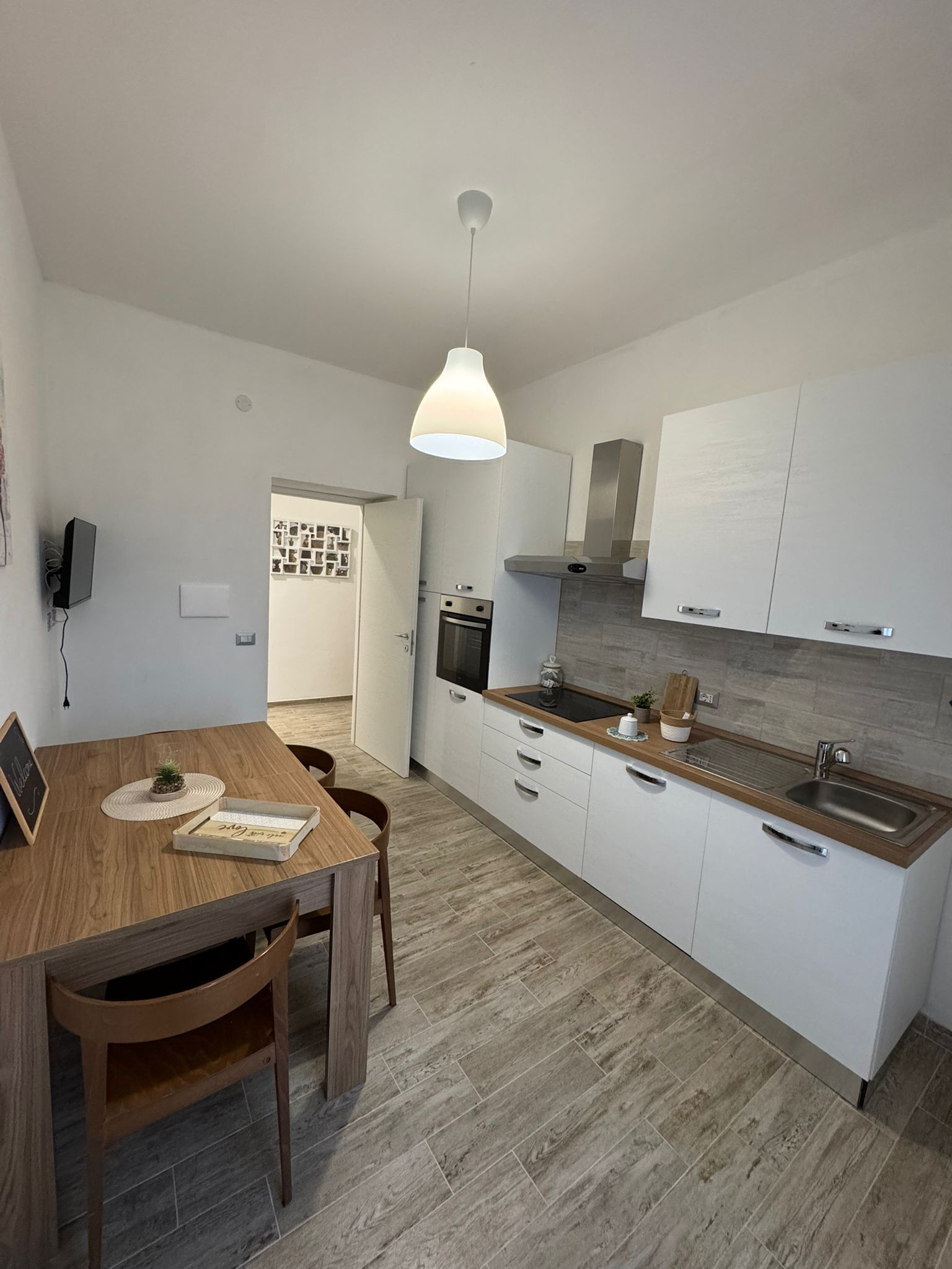 Een moderne keuken met witte kasten, een houten eettafel en een hangende吊灯.