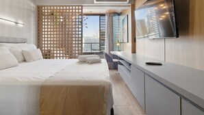 Moderni hotellihuone, jossa on sänky, televisio, työpöytä ja näkymä kaupunkiin.