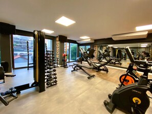 A gym with various exercise equipment, large windows, and a mirror reflecting the equipment.