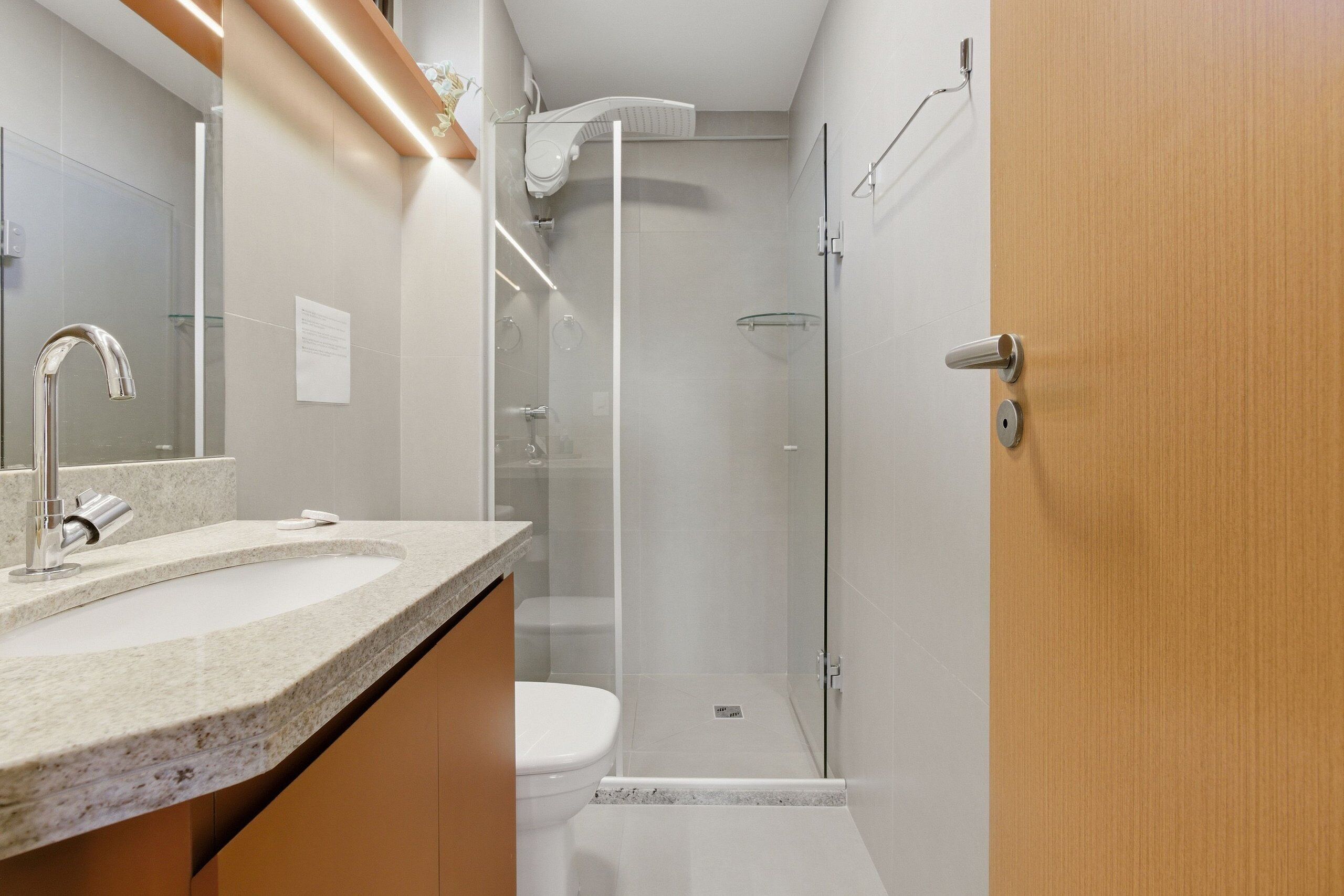 A modern bathroom with a glass shower enclosure, a toilet, and a sink with a granite countertop.