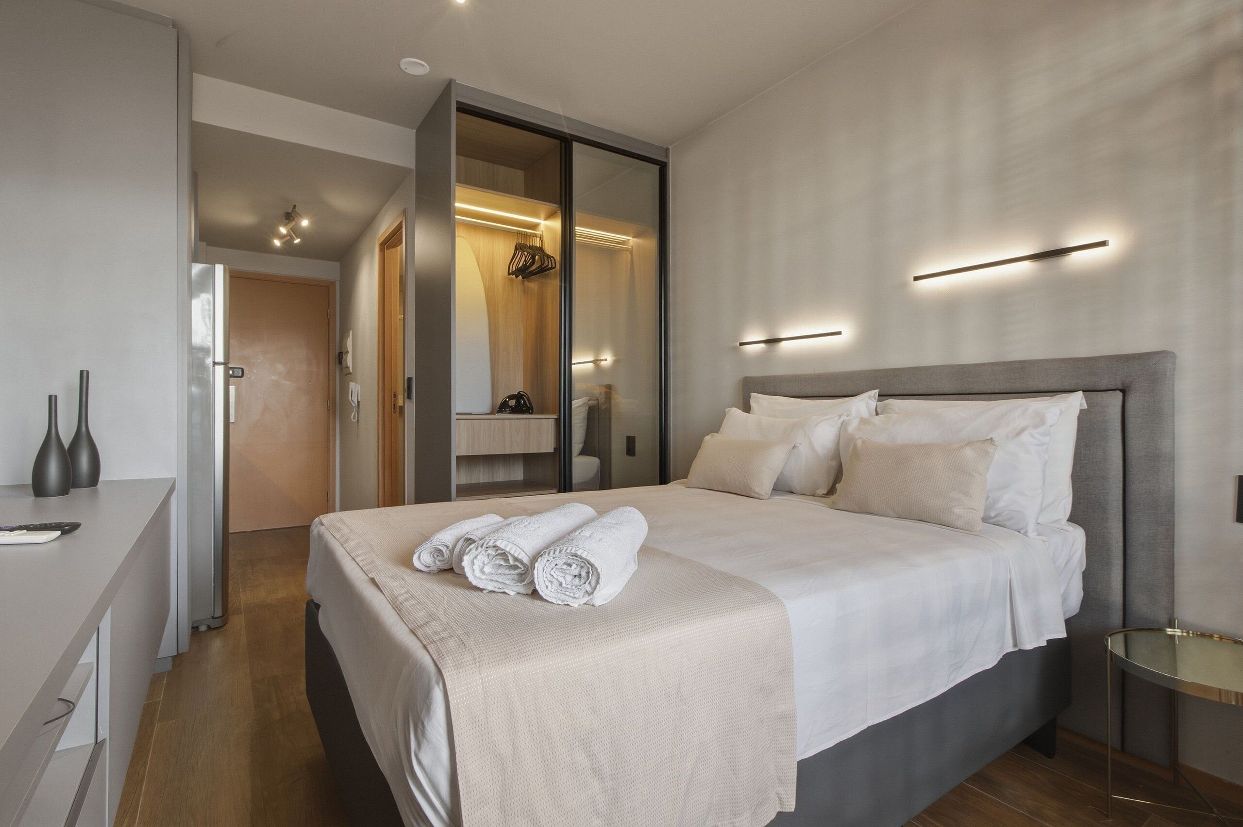Una habitación de hotel moderna con una cama grande, un escritorio, un armario y un espejo.