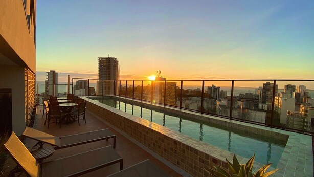 Kattouima-allas, josta avautuu näkymä kaupunkiin, ruokailualue, jossa on tuoleja ja pöytiä, sekä portaikko, joka johtaa uima-altaalle.