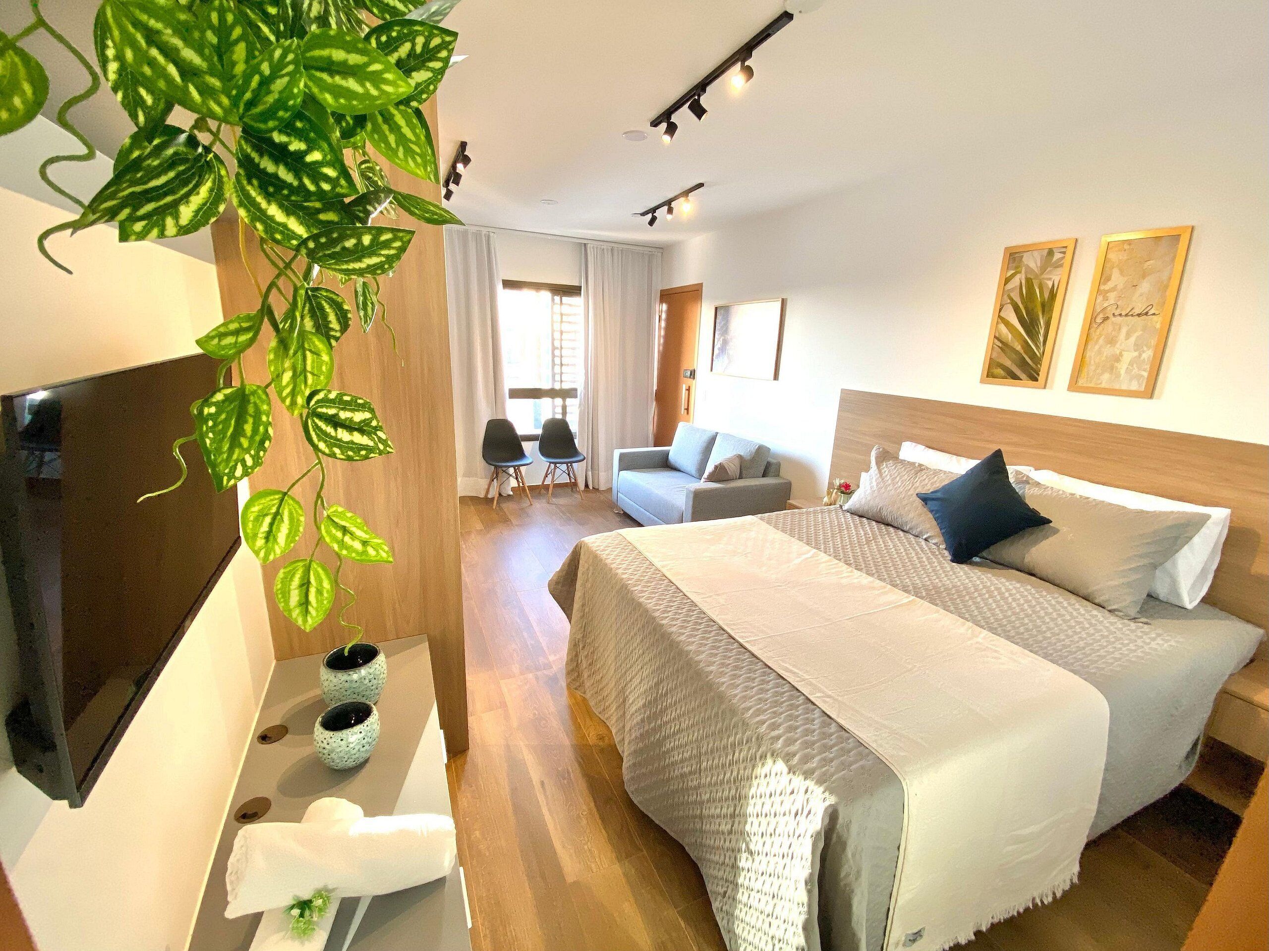 A hotel room with a bed, a TV, a desk, two chairs, and a potted plant.