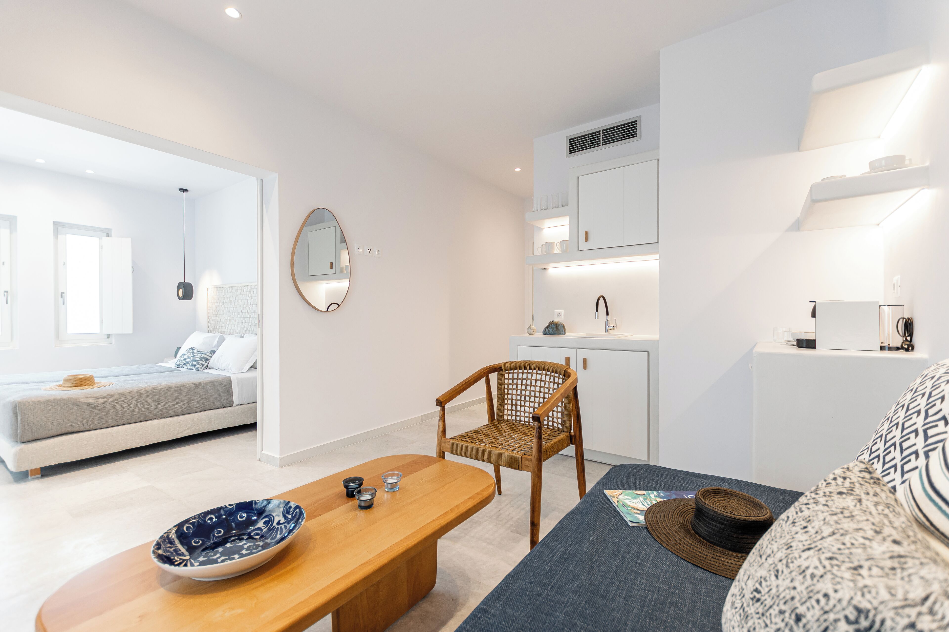 A modern, well-lit room with a bed, a dining table, a chair, and a kitchen area.