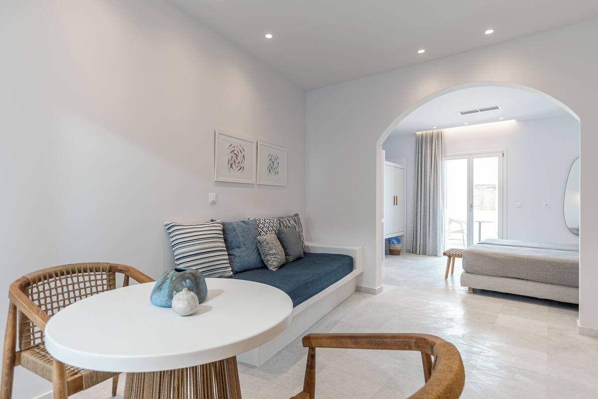 Ein modernes Wohnzimmer mit einem runden weißen Tisch, einem blauen Sofa mit gemusterten Kissen und einem Holzstuhl.