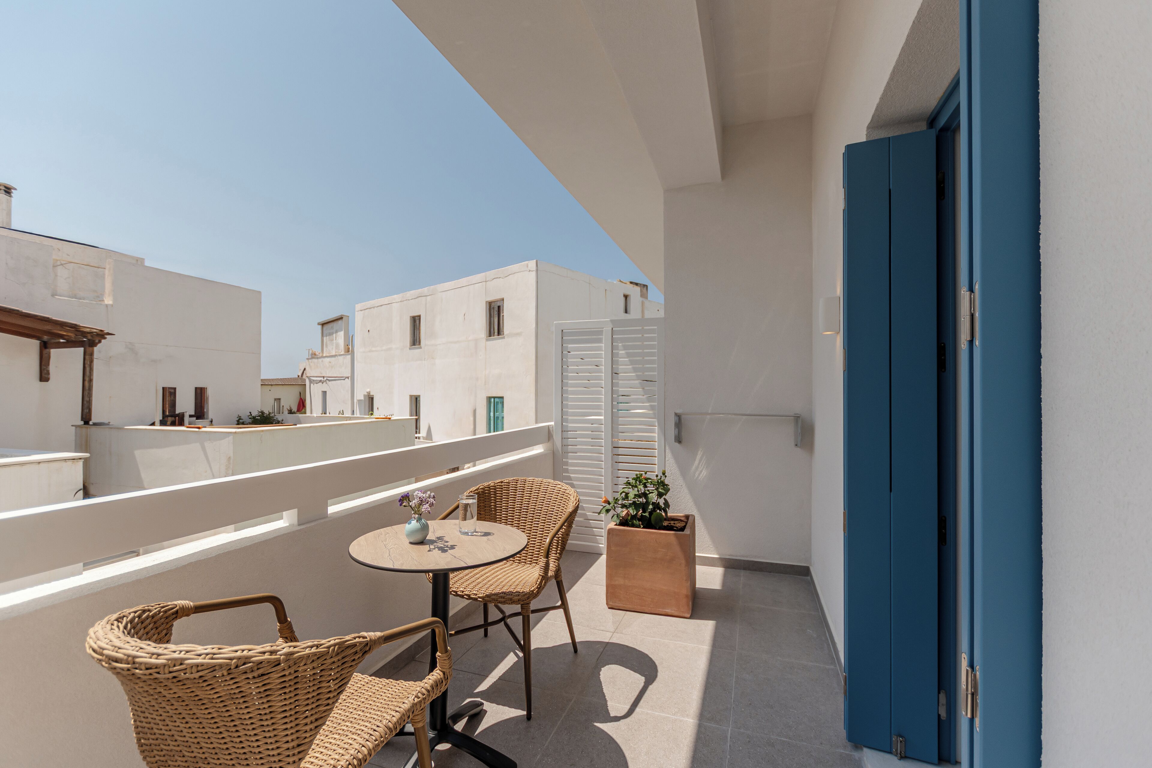 A balcony with wicker chairs and a small table, white walls, and a blue door.