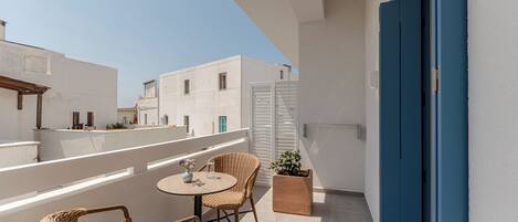 A balcony with wicker chairs and a small table, white walls, and a blue door.