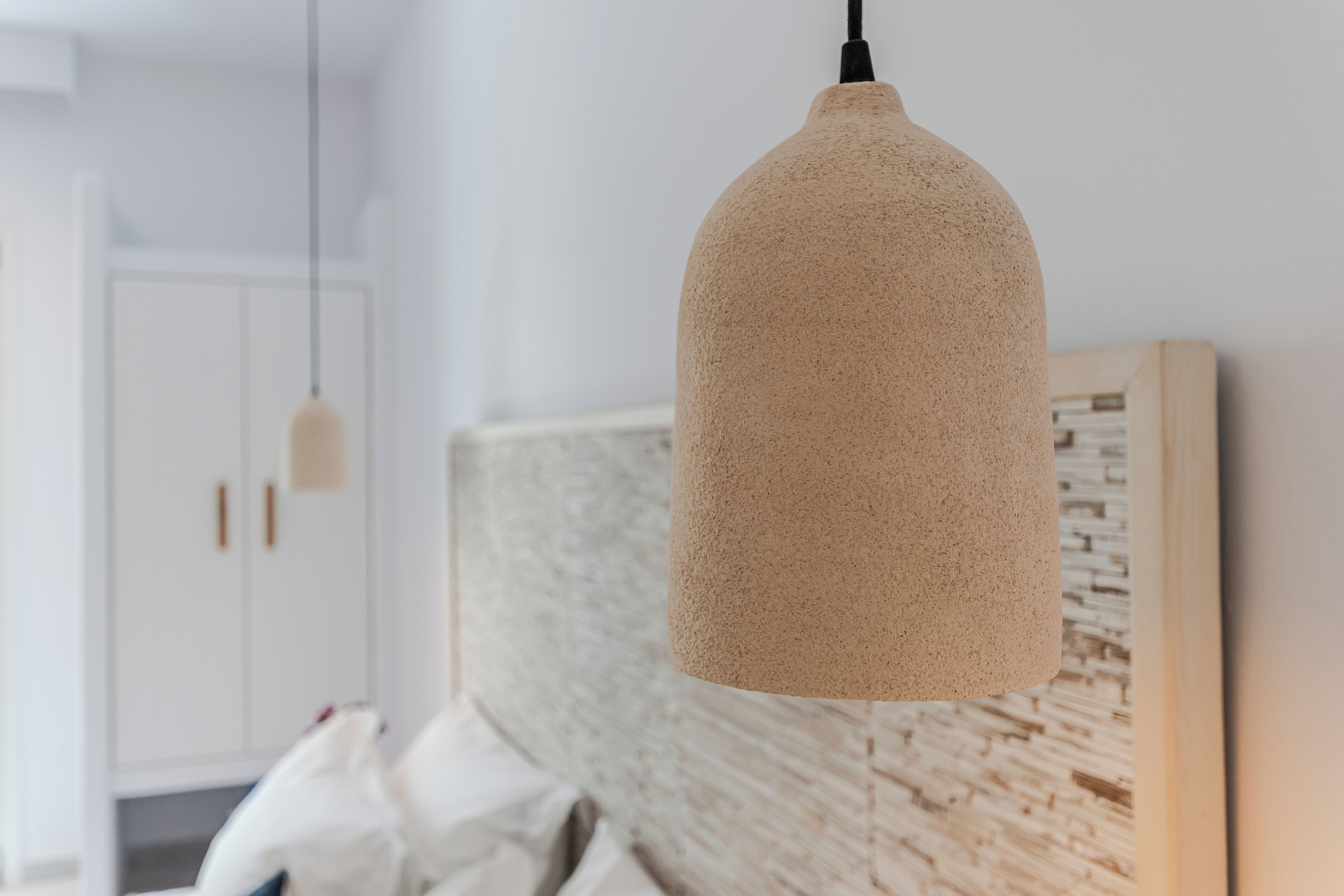 A modern room with a textured pendant light, a wooden headboard, and a white wardrobe.