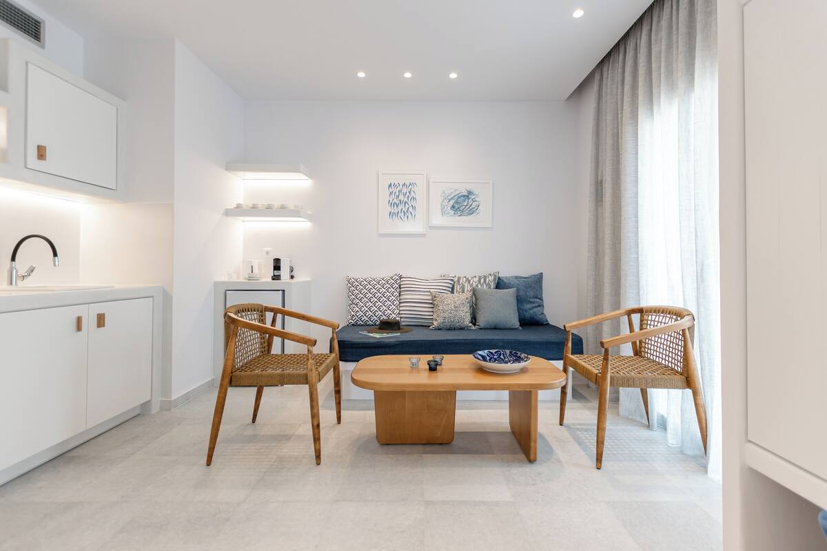Ein modernes Wohnzimmer mit einer Couch, zwei Korbstühlen, einem Couchtisch und einer Küchenzeile mit Schränken und einer Spüle.