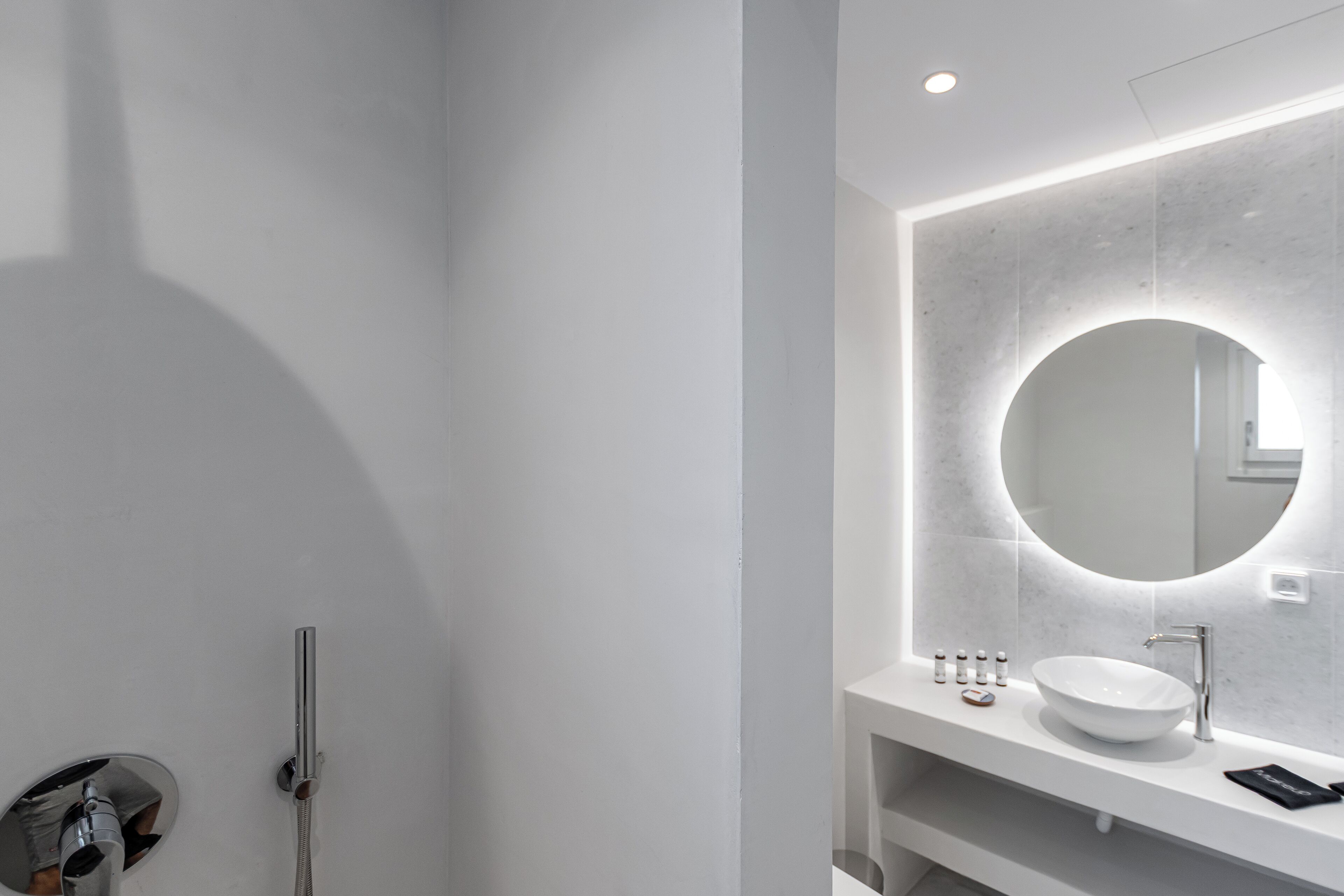 A modern bathroom with a round mirror, a white sink, and a handheld showerhead.