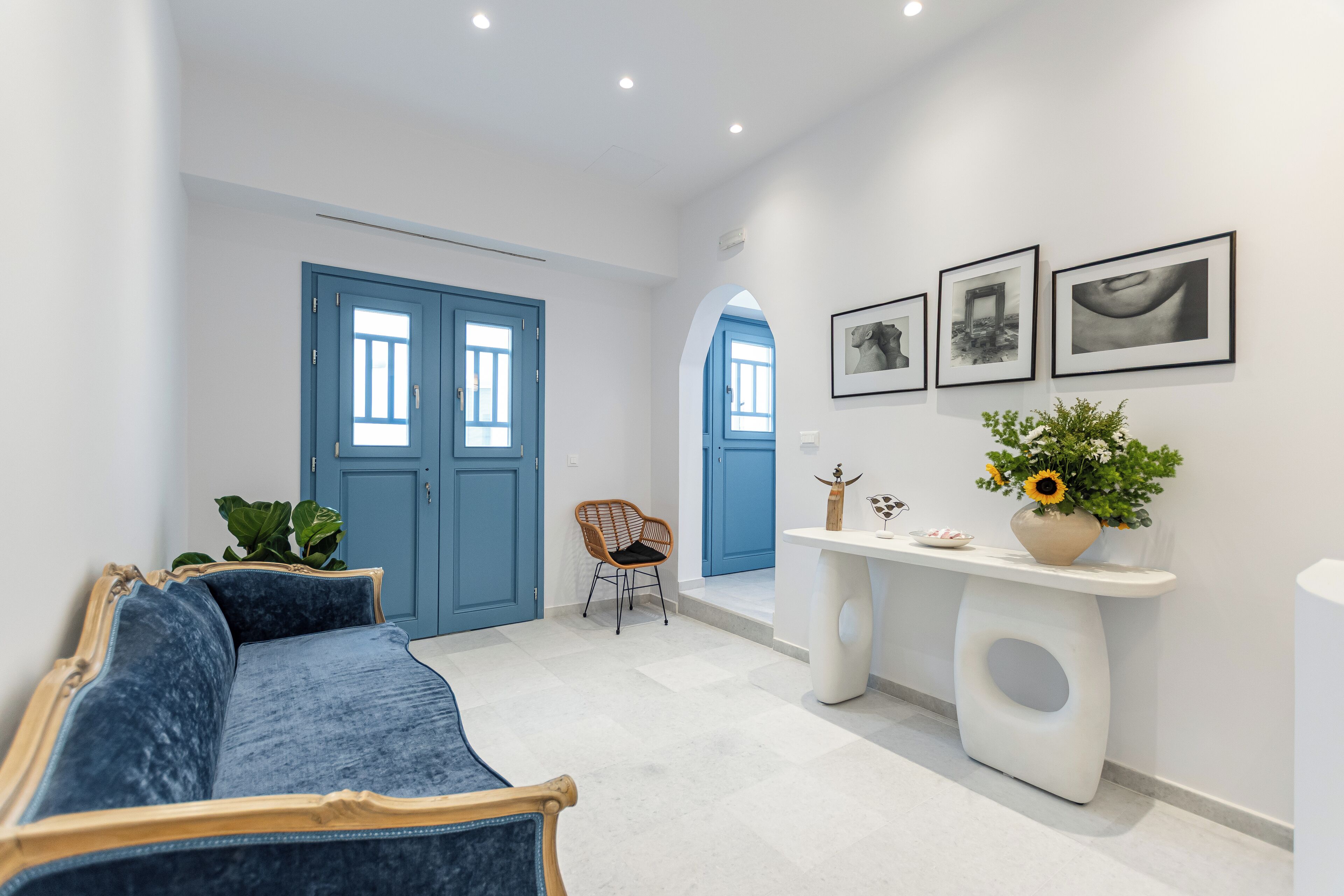 A modern hallway with a blue sofa, a white console table with a vase of flowers, and framed pictures on the wall.