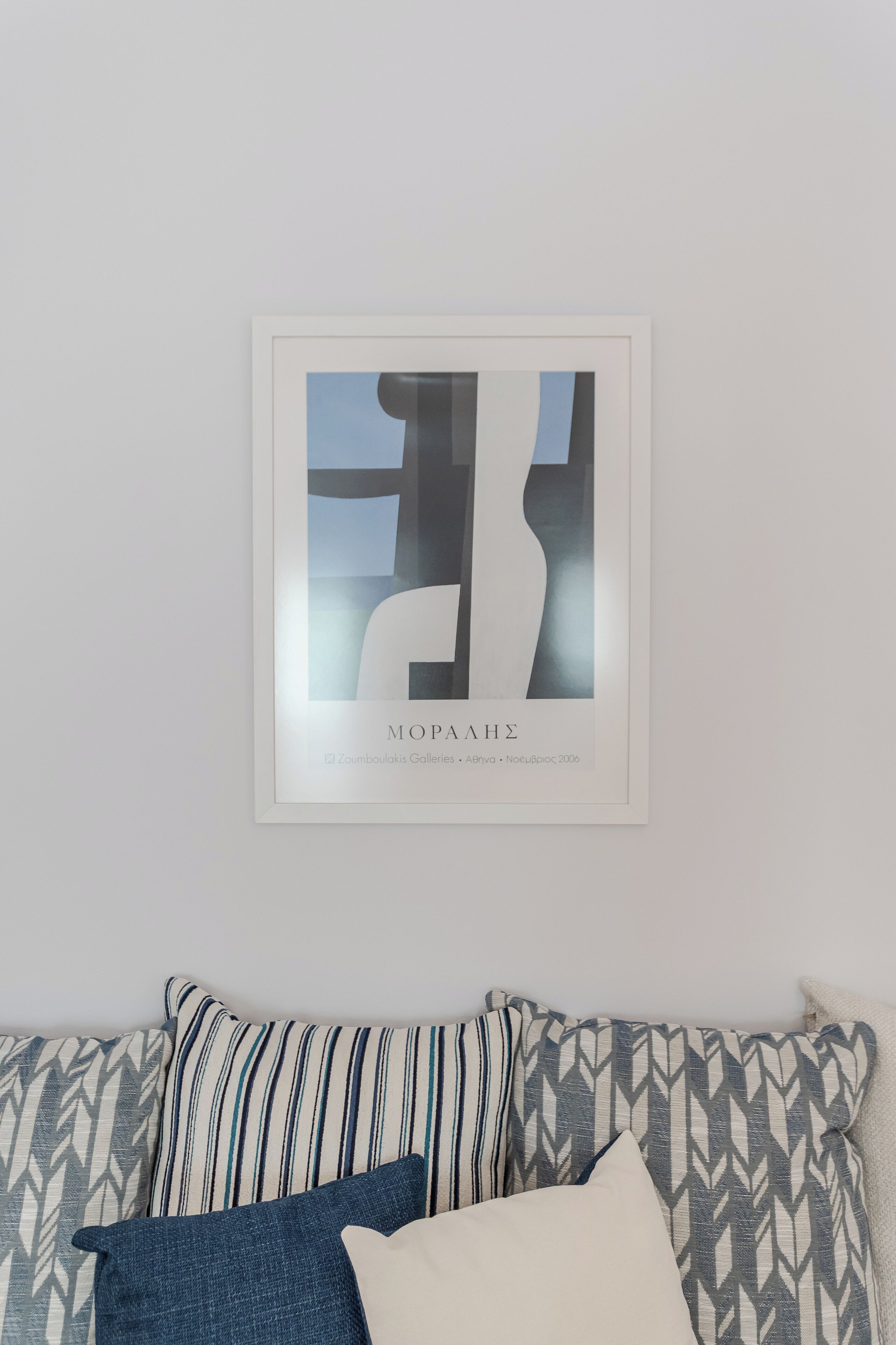 Una obra de arte enmarcada titulada "MOPAAHÉ" de Zomboulakis Galleries, exhibida sobre un sofá con estampado y cojines.