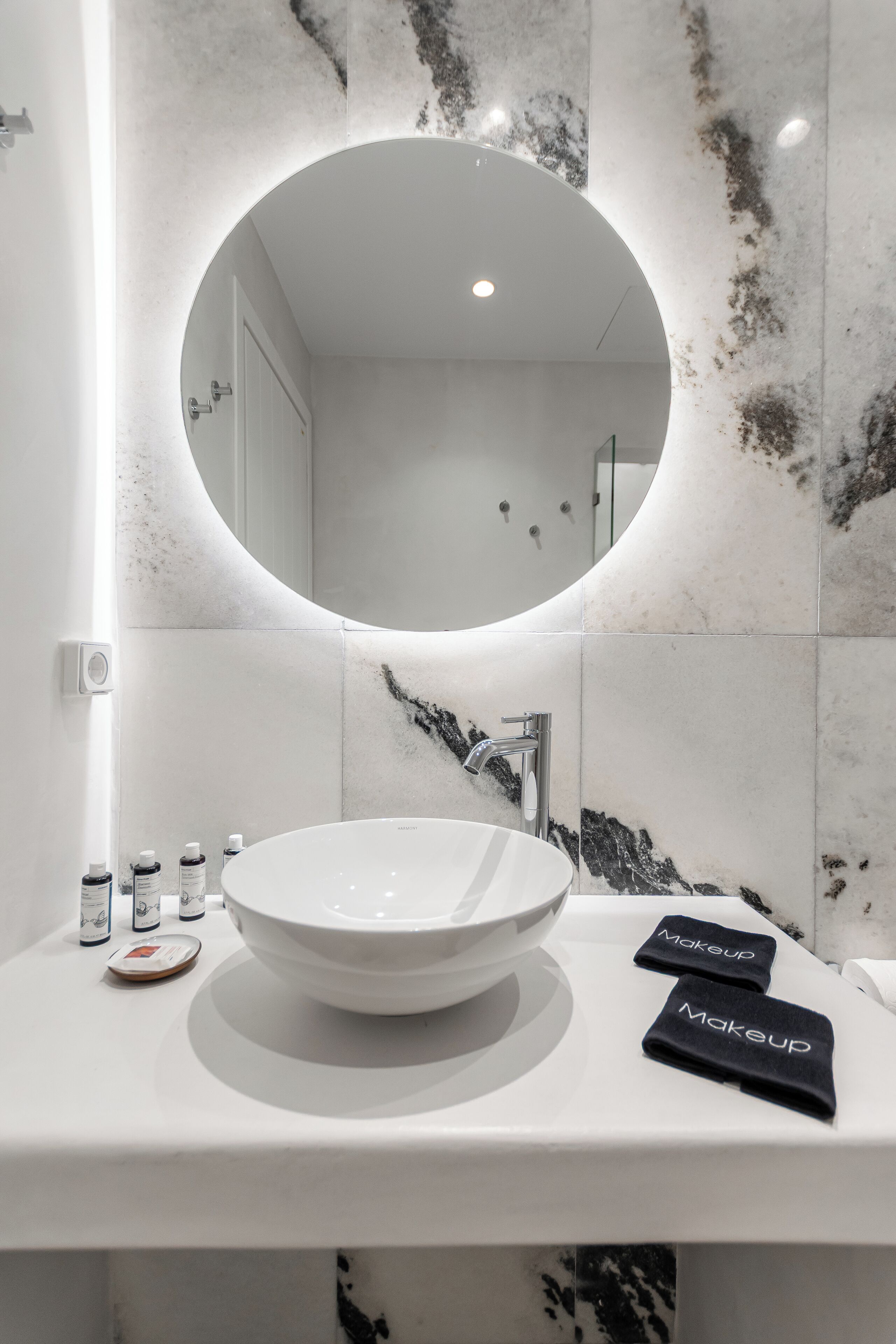 Un baño moderno con un espejo redondo, lavamanos blanco y azulejos de mármol.