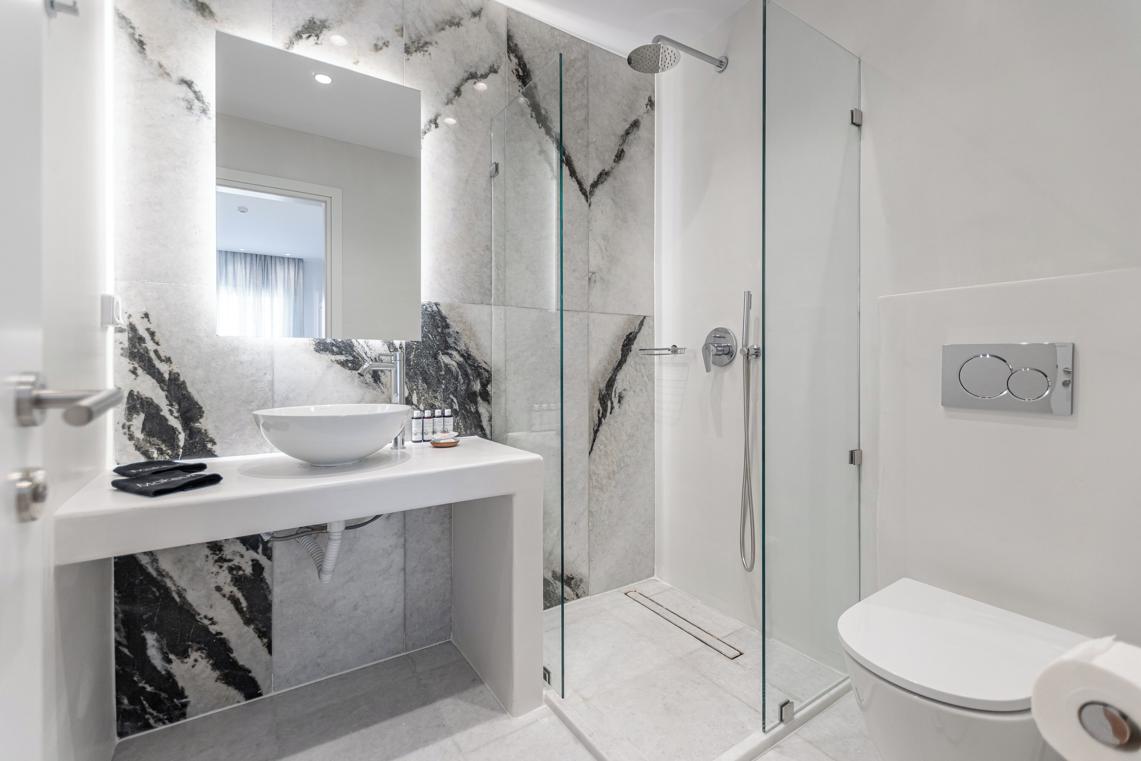 A modern bathroom with a marble vanity, a glass shower enclosure, and a toilet.