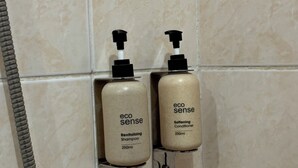 Deux bouteilles de shampoing et d’après-shampoing de la marque « Eco Sense » sont fixées au mur dans une salle de bain.