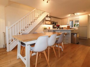 A modern kitchen with a wooden dining table, white chairs, and a staircase. - Poldreth (Truro)