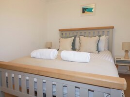 Una cama bien hecha con dos toallas blancas, un cabecero de madera y un pequeño cuadro enmarcado con una imagen de una playa en la pared.