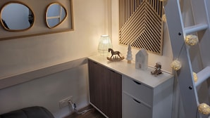 Een moderne slaapkamer met een witte kaptafel, een houten plafond, een spiegel, een geometrisch wandpaneel, een klein schommelpaard en een ladder.