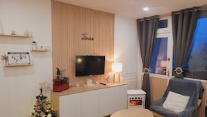 Een moderne woonkamer met een flatscreen televisie, een tafeltje, een stoel, een kerstboom en een open haard.