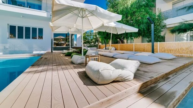 A poolside area with wooden decking, lounge chairs, and umbrellas. - Stylish & Bright Gem ~ Walk to Beach, Patio, Pools (Paralimni)
