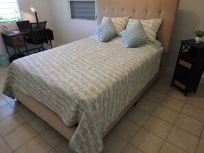 Un dormitorio con una cama, un escritorio con una computadora portátil y una pequeña mesa con una planta.