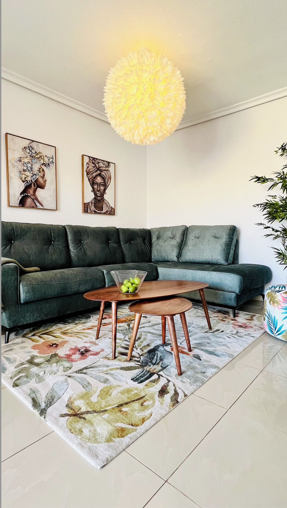 Sala de estar con un sof á verde, una mesa de centro de madera con manzanas, un tapete floral y dos cuadros en la pared.