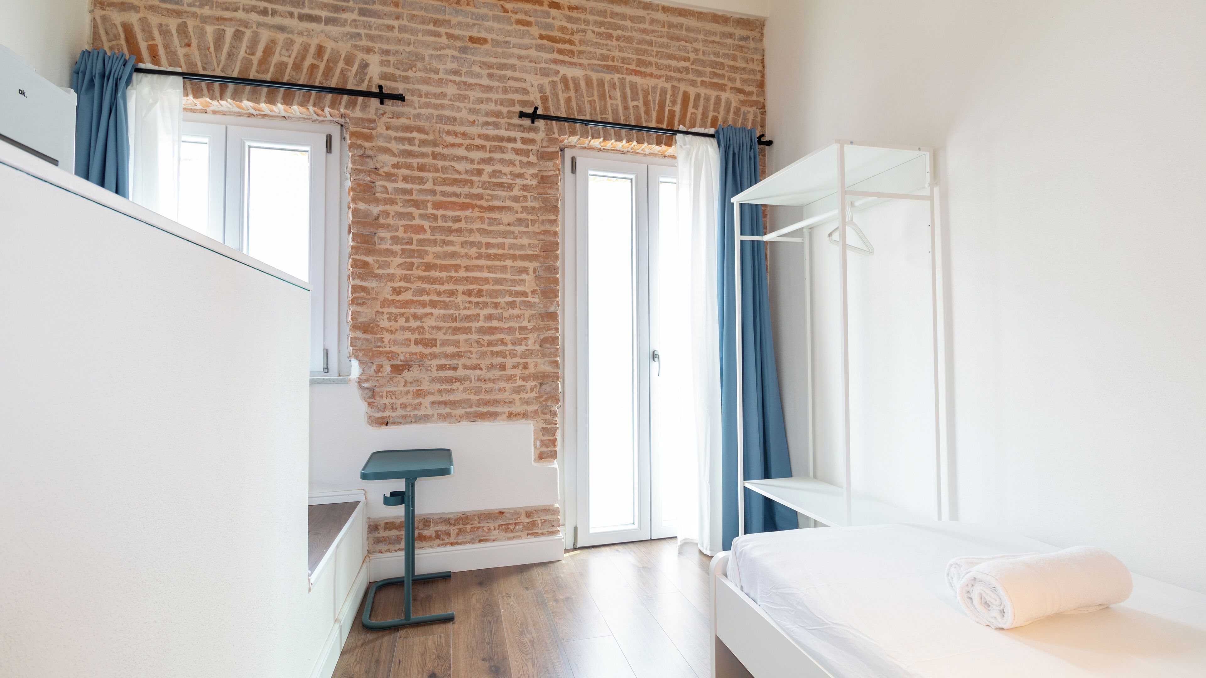 A bedroom with a brick wall, a bed, a desk, and a wardrobe.