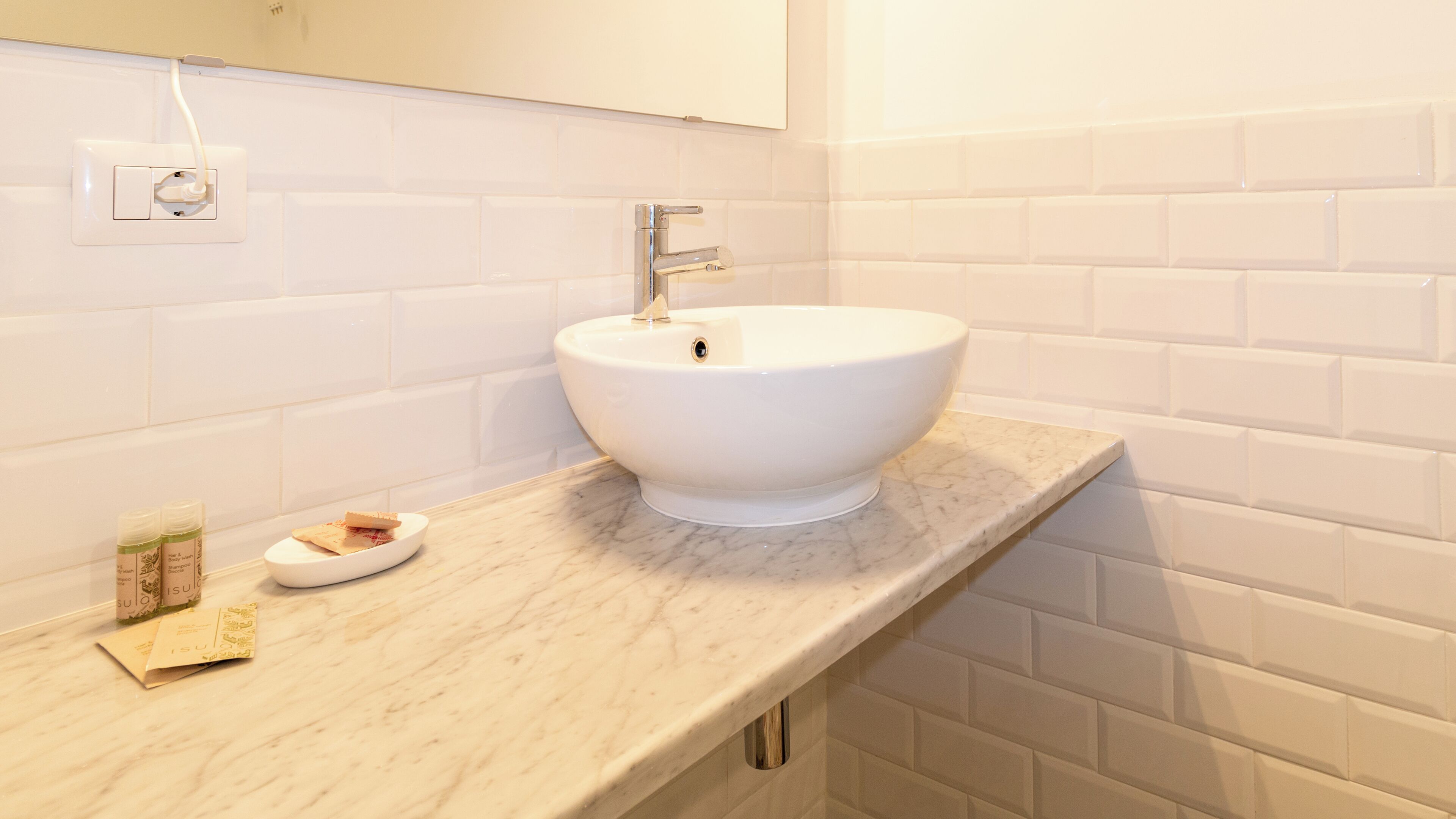 Une salle de bain avec un lavabo blanc, un comptoir en marbre et des carreaux de céramique blancs rectangulaires sur les murs.