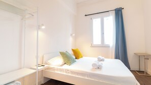 Un letto rifatto con cuscini e asciugamani, un comodino con un telefono, una finestra con tende e un piccolo tavolino.