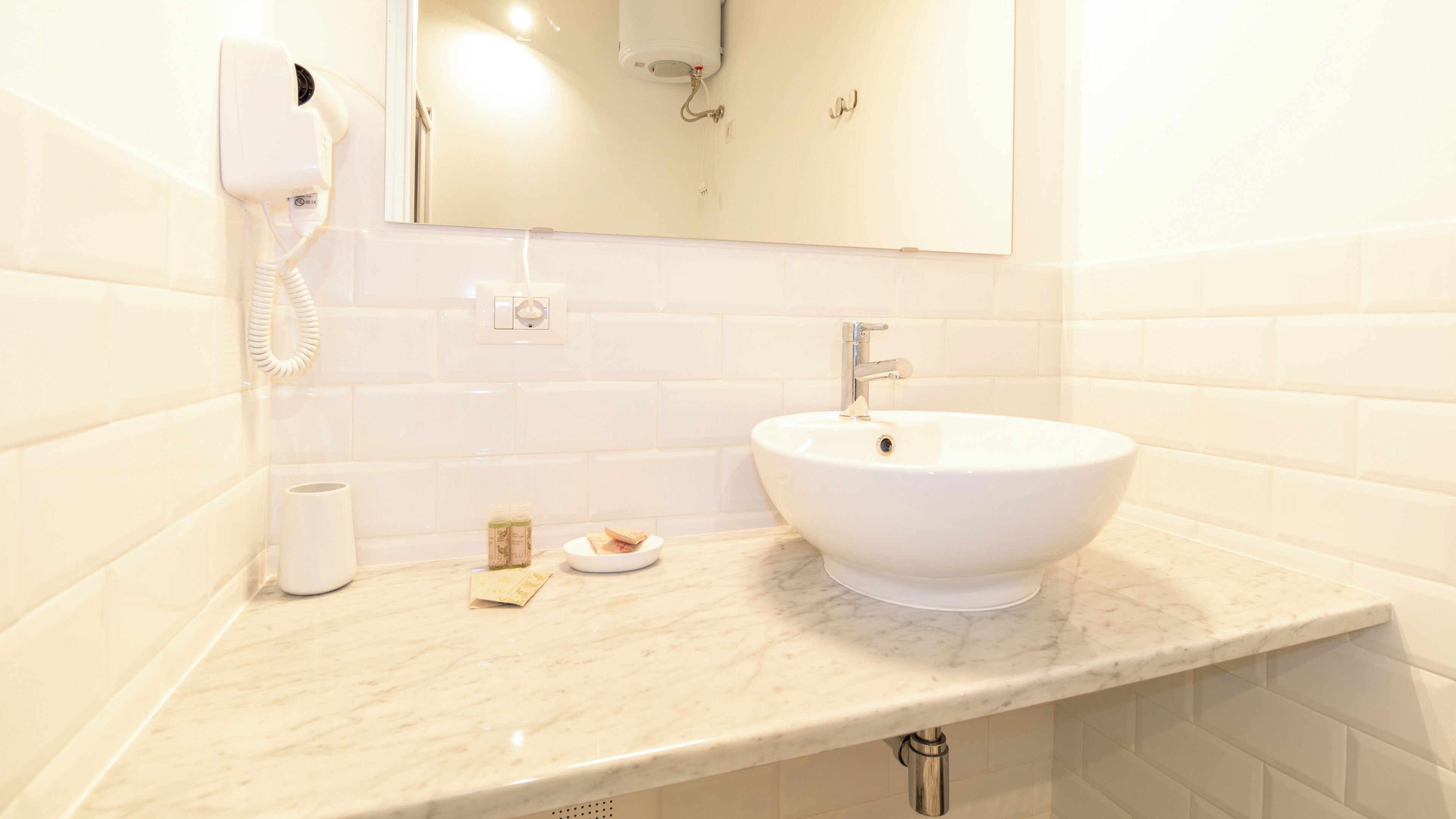 A bathroom with a white sink, a mirror, a hairdryer, and a towel dispenser.