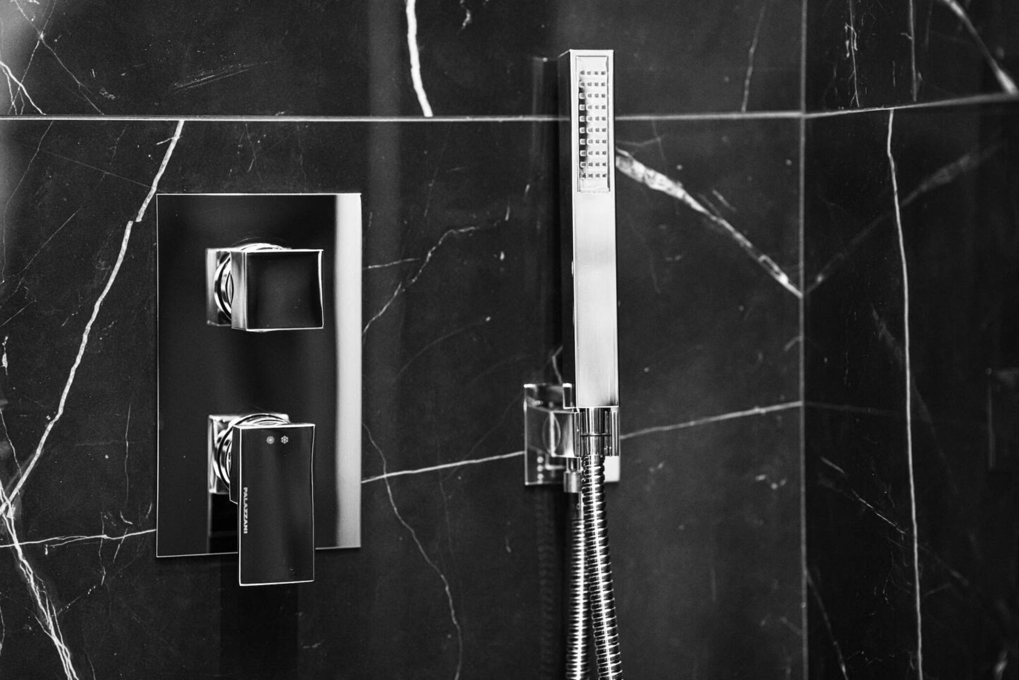 Ein modernes Badezimmer mit schwarzer Marmorwand, einer Handbrause und einer wandmontierten Bedienung.