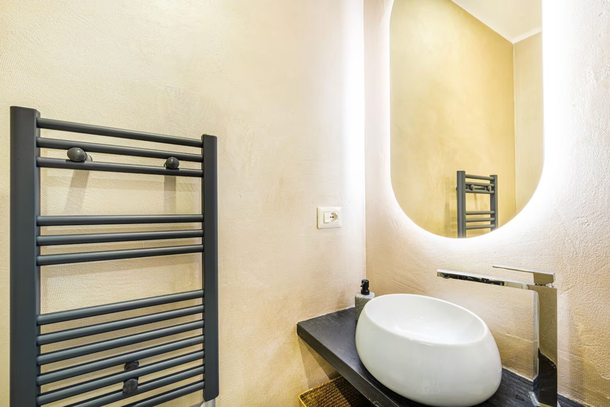 Une salle de bain avec un porte-serviettes noir, un lavabo blanc et un miroir adossé à un mur incurvé.