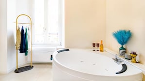 A modern bathroom with a freestanding bathtub, a towel rack with clothes, a window with blinds, and decorative items on the vanity. - Vatican City Deluxe (Rome)