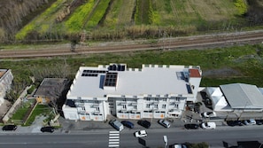 Ein mehrstöckiges Gebäude mit flachem Dach, Solaranlagen und einem Parkplatz mit mehreren Autos.
