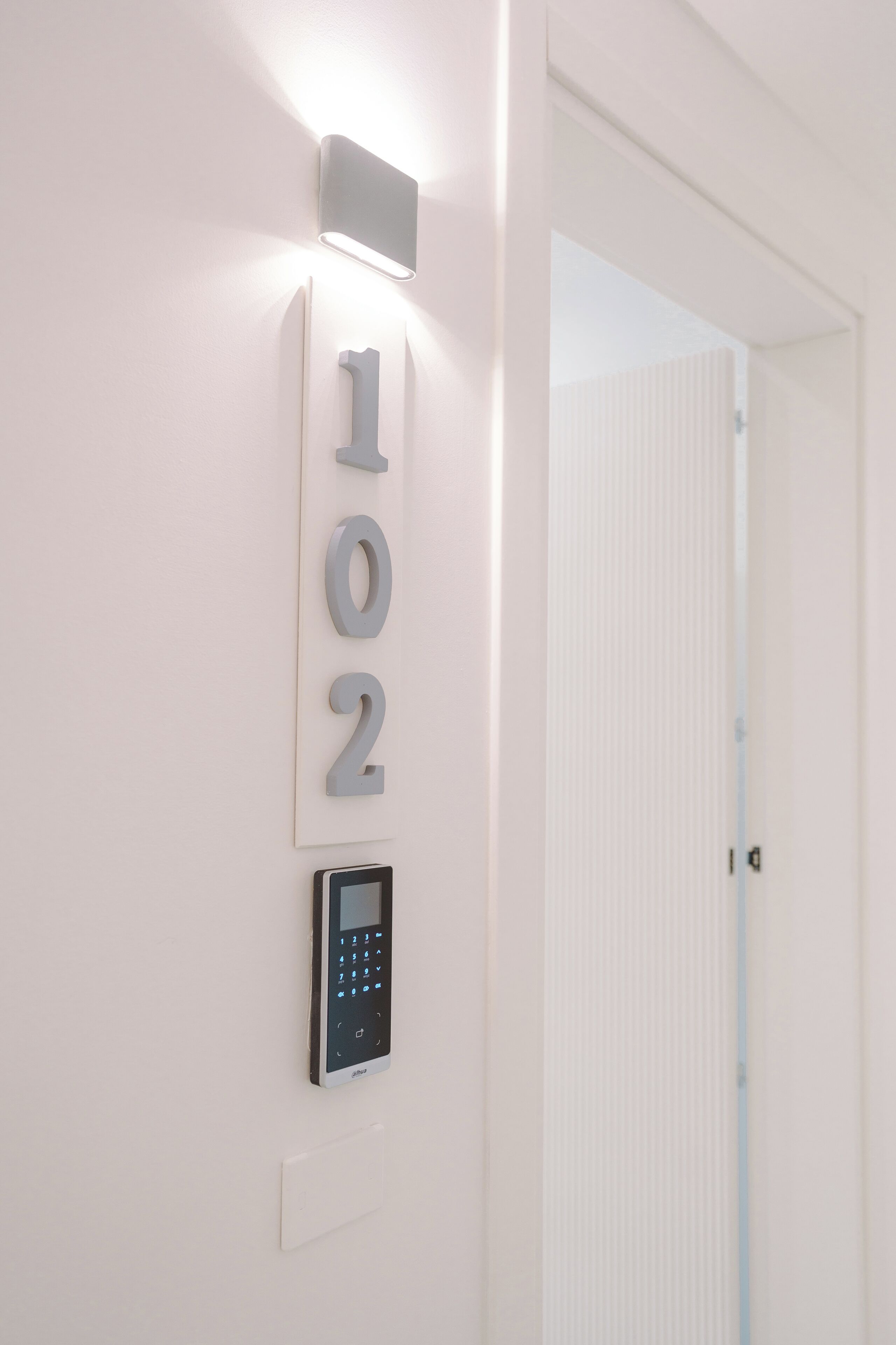 A wall-mounted number display and a keypad, likely for room access, in a hallway with a white door.
